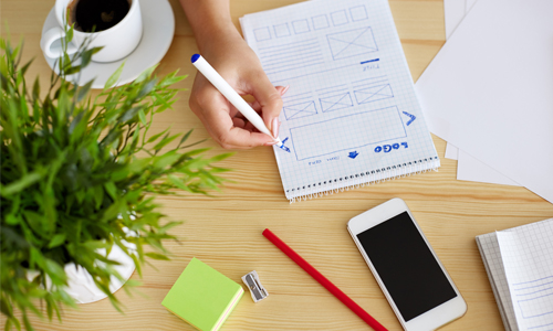 Photo depicts a woman sketching layout ideas for a website.